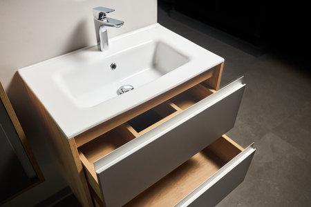 Solutions for placing things in bathroom horizontal sliding pull out drawer shelves storage in a cupboard under stoneware washbasin cabinet under sink and faucet. Modern loft flat minimalistic design.の写真素材