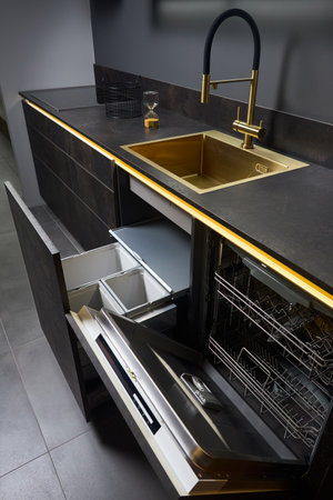 Dishwasher and kitchen waste bin cabinet. Pull out kitchen drawers for waste bin separate waste collection and Dishwasher under golden sink basin and facet black glass electric hob stoneware toptable.の写真素材