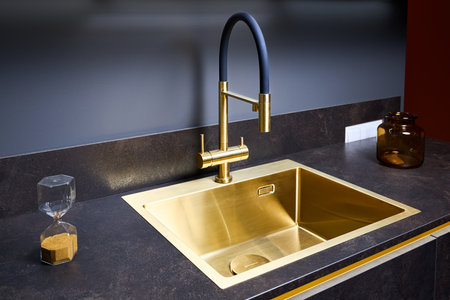 Luxurious interior square golden brass sink and faucet double tap mixer in contemporary modern design with stone marble stoneware countertop black and gold kitchen with sandwatch and glass pot.の写真素材