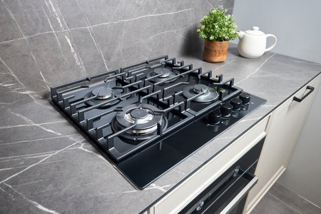 Modern hob gas stove made of tempered black glass using natural gas or propane for cooking products on light countertop in kitchen interior with oven tea pot and flowers.の写真素材