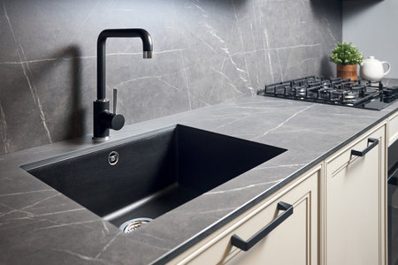 Kitchen sink area with black square matte sink tap in contemporary style. Matte black and stoneware kitchen design. Black ceramic sink with gas hob and oven in background.の写真素材