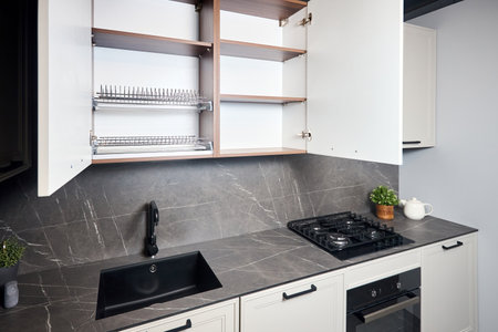 Interior of white and grey kitchen, horizontal linear layout. Luxury modern fitted flat design kitchen with opened cupboard shelves sideboard with dish drying cabinet.の写真素材