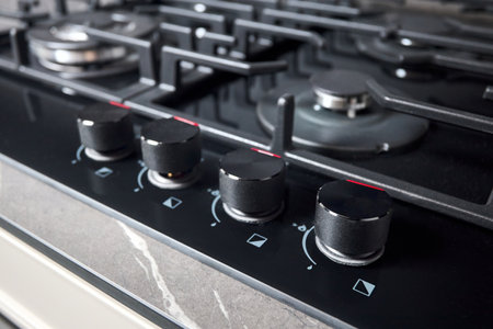 Control knobs with auto ignition selective focus closeup over out of focus black tempered glass gas stove cooker hob with wok burner built in compact high pressure laminate HPL countertop.の写真素材