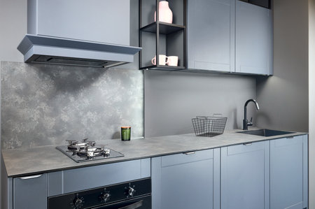 Blue grey contemporary kitchen linearlayout with hood two burners gas cooker hob oven and built in dishwasher machine and square black sink and tap compact high pressure laminate HPL countertop.の写真素材