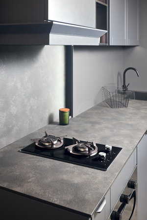 Contemporary black tempered glass gas stove hob with Two burners with auto ignition knob cast iron pan supports fan hood and square black sink built in compact high pressure laminate HPL countertop.の写真素材