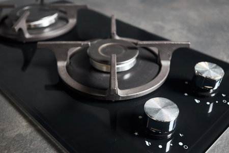 Contemporary black tempered glass gas stove hob with Two burners with auto ignition knob cast iron pan supports built in compact high pressure laminate HPL countertop closeup macro view.の写真素材