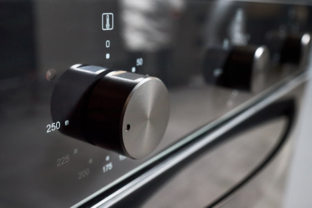 Oven knob selective focus stainless steel turned to 250 Celsius degrees over black glass front panel of contemporary modern kitchen bakery professional cooker closeup shot with copyspace.の写真素材