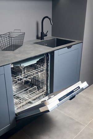 Opened empty dishwasher machine in contemporary blue grey kitchen with compact high pressure laminate HPL countertop and black square sink and tiled floor.の写真素材