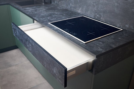 Induction cooker black tempered glass hob aspirating induction hob on marble stoneware countertop with horizontal sliding pull out drawer shelf storage in kitchen cupboard.の写真素材