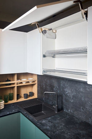 System for bi-fold fronts and facades for kitchen cabinets direct access with lifting mechanism closeup. Fitted flat design kitchen with sink tap and opened cupboard sideboard dish drying cabinet.の写真素材