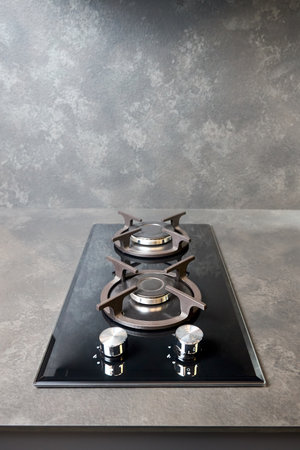 Contemporary black tempered glass gas stove hob with Two burners with auto ignition knob cast iron pan supports and flame safety valve built in compact high pressure laminate HPL countertop.の写真素材
