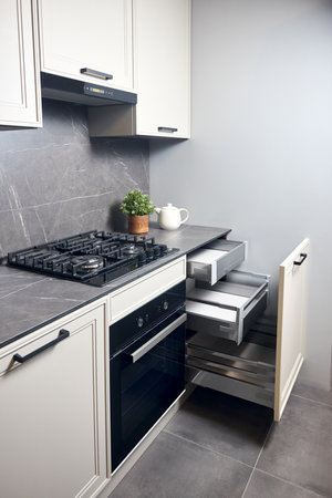 Gas cooker black glass and iron hob and hood on marble light stoneware countertop with horizontal sliding pull out drawer shelves storage in kitchen cupboard.の写真素材