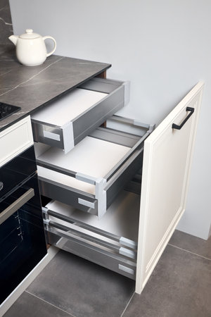 Gas cooker black glass and iron hob on marble light stoneware countertop with horizontal sliding pull out drawer shelves storage in kitchen cupboard.の写真素材
