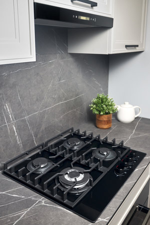 Contemporary black tempered glass gas stove hob with four burners with auto ignition knob cast iron pan supports fan hood and square black sink built in compact high pressure laminate HPL countertop.の写真素材
