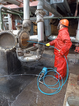 Man cleaning condenser tubes removing scales of petrochemical industrial heat exchanger with high pressure water jetting machine wear helmet and protective clothing for water jetting.の写真素材