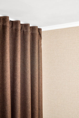 Curtains made of brown matting fabric hang on the ceiling cornice near the wall papered with a matting texture or rough canvas under a white plasterboard ceiling with ceiling baseboards vertical shot.の写真素材