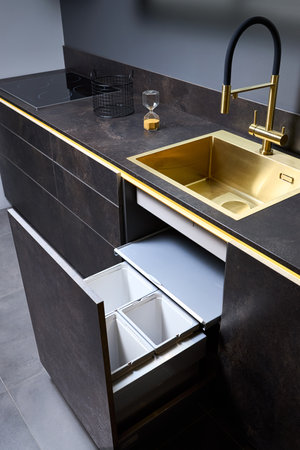 Kitchen waste bin cabinet. Pull out kitchen drawer for waste bin separate waste collection under golden sink basin and faucet black glass electric hob stoneware toptable contemporary flat designの写真素材