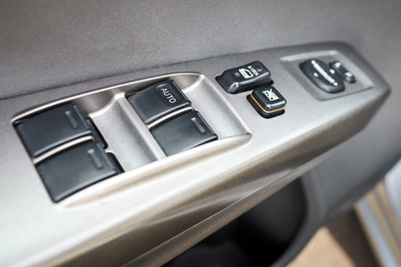 Modern hybrid electric car closeup interior detail. Driver door control panel in armrest with window...