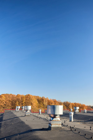 Air roof exhaust ventilation fan system of industrial large commercial building. Hooded chimneys flues and ducts in row on rooftop, selective focus vertical shot with lightning protection system.の写真素材