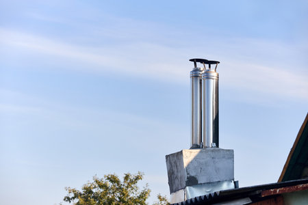 Two modern style chimneys from oven and fireplace stacked stainless steel on rural house roof covered with slate under clear blue sky with copyspace.の写真素材