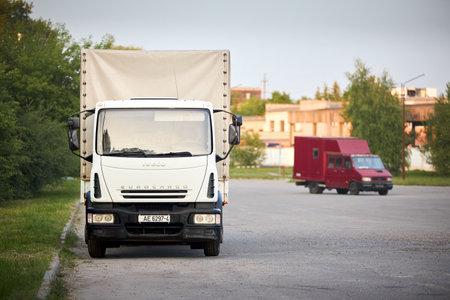 Minsk, Belarus - May, 28 2023: Iveco EuroCargo 120E21 Second generation 2002-2015 medium duty truck produced by Italian manufacturer Iveco. White truck with out of focus red Iveco Daily on background.のeditorial素材