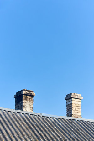 White old chimney with traces of soot made of white bricks is on rural house roof covered with slate, under clear blue sky with copyspace vertical shot.の写真素材