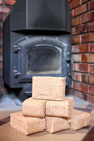 Fuel briquettes made of birch and oak alternative eco-friendly fuel for the fireplace in the house. Fuel briquettes lay near steel stove with tiled floor cottage interior vertical.の写真素材