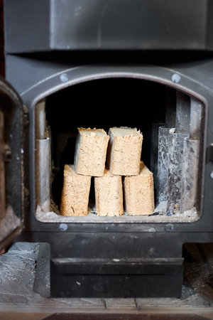 Fuel briquettes made of birch and oak alternative eco-friendly fuel for fireplace in house. Fuel briquettes lay into steel stove with tiled floor cottage interior.の写真素材