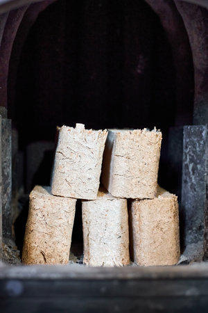 Fuel briquettes made of birch and oak alternative eco-friendly fuel for fireplace in house. Fuel briquettes lay into steel stove with tiled floor cottage interior.の写真素材