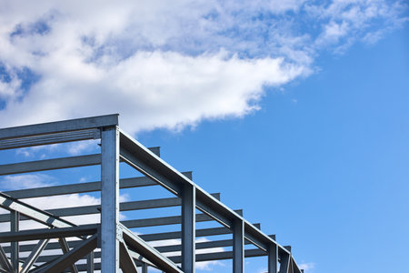 Metal construction. Urban geometrical interlacing of bolted connections cross bars and beams of construction site over blue sky with clouds copyspace background.の写真素材