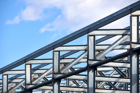 Metal construction. Urban geometrical interlacing of bolted connections cross bars and beams of construction site over blue sky with clouds copyspace background.の写真素材