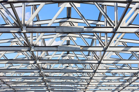 Metal construction texture pattern. Urban geometrical interlacing of bolted connections cross bars and beams of construction site over blue sky with clouds background.の写真素材