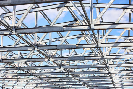 Metal construction texture pattern. Urban geometrical interlacing of bolted connections cross bars and beams of construction site over blue sky with clouds background.の写真素材