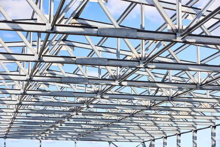 Metal construction texture pattern. Urban geometrical interlacing of bolted connections cross bars and beams of construction site over blue sky with clouds background.の写真素材