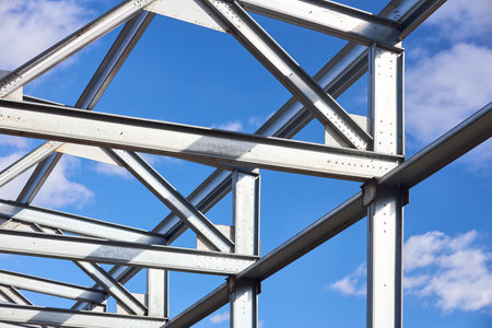 Metal construction textured pattern. Urban geometrical interlacing of bolted connections cross bars beams and supporting structures of construction site over blue sky with clouds background.の写真素材