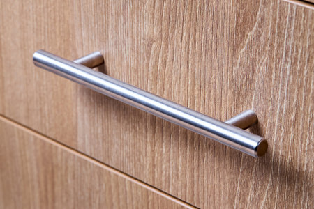 Rectangle shaped kitchen cabinet with stainless steel brushed handles close up selective focus shot. Cabinet door adorned with metal handlesの写真素材