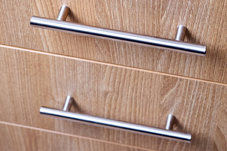 Rectangle shaped kitchen cabinet with stainless steel brushed handles close up selective focus shot. Cabinet door adorned with metal handlesの写真素材