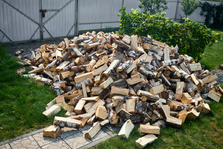 Stack of birch firewood with hand chopping block. Chopped firewood for winter. Lot of firewood - harvesting wood for heating the house. Horizontal photo. Chopped firewood on grass in yard.の写真素材