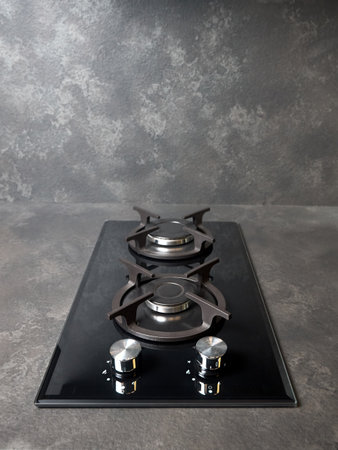 Contemporary black tempered glass gas stove hob with Two burners with auto ignition knob cast iron pan supports and flame safety valve built in compact high pressure laminate HPL countertop.の写真素材