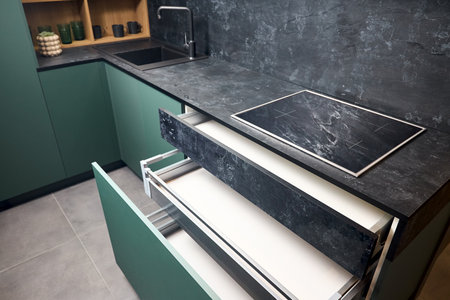 Induction cooker black tempered glass hob aspirating induction hob on marble stoneware countertop with horizontal sliding pull out drawer shelf storage in kitchen cupboard.の写真素材