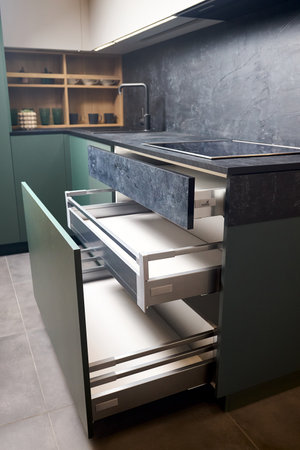 Induction cooker black tempered glass hob aspirating induction hob on marble stoneware countertop with horizontal sliding pull out drawer shelf storage in kitchen cupboard.の写真素材