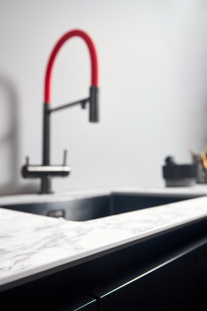 Closeup shot of contemporary kitchen countertop made of compact high pressure laminate HPL selective focus, with out of focus background with square basin and red tap.の写真素材