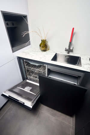 Kitchen with built-in opened dishwasher and pull out drawer for waste bin separate waste collection. Water faucet sink built in compact high pressure laminate HPL countertop undermount installation.の写真素材