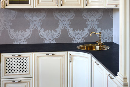 Interior of modern classic style kitchen in beige colors with golden sink basin. Drawers cabinets with lattice and golden ornamental decoration. Dark stoneware empty countertop.の写真素材