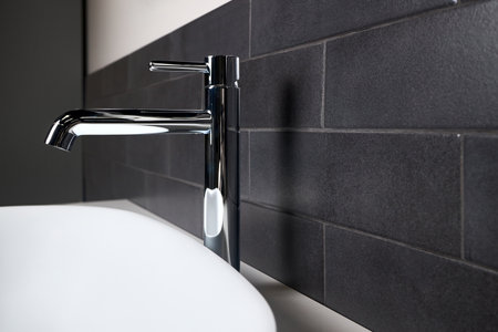 Interior detail of bathroom with washbasin sink with oval mounted overhead sink and faucet. Bathroom interior sink with black tiled wall modern flat minimalistic design side view close up copy space.の写真素材