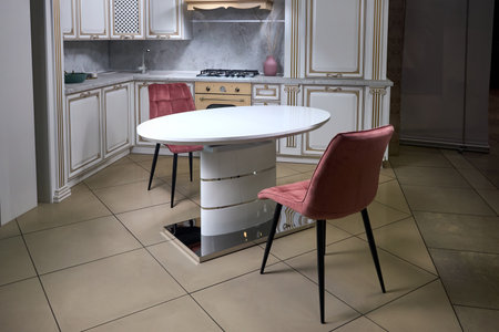 Interior of modern kitchen in classic style with golden elements in beige colors with built-in appliances gas hob electric oven stone sink and extractor fan with transformer kitchen table, two chairs.の写真素材
