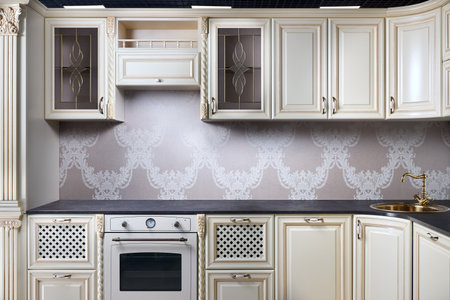 Interior of modern classic style kitchen in beige colors with golden sink basin. Drawers cabinets with lattice and golden ornamental decoration. Dark stoneware empty countertop.の写真素材