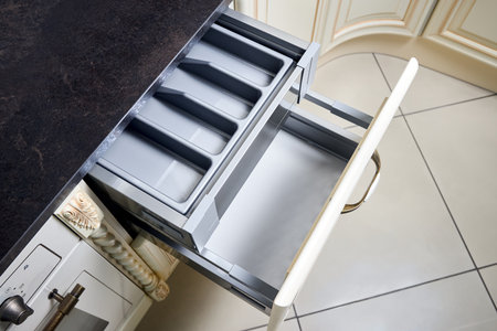 Solutions for placing utensils in classic kitchen - horizontal sliding pull out drawer shelves storage in a cupboard for kitchenware cookware under stoneware countertop white gas hob, with copy space.の写真素材
