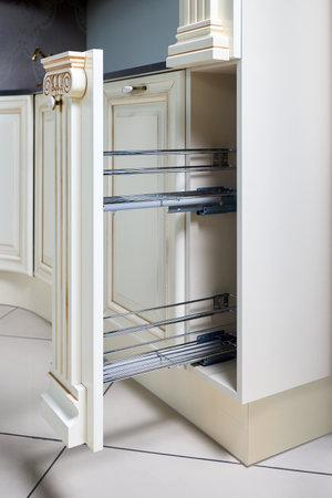 Pull out spice rack cabinet filler pantry. Interior of modern kitchen in classic style with golden elements in beige colors. Vertical drawer for spices shelf under countertop with front wooden panel.の写真素材