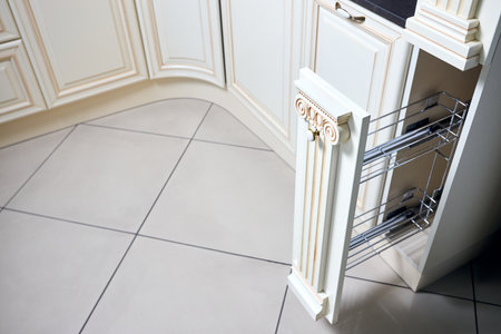 Pull out spice rack cabinet filler pantry. Interior of modern kitchen in classic style with golden elements in beige colors. Vertical drawer for spices shelf under countertop with front wooden panel.の写真素材